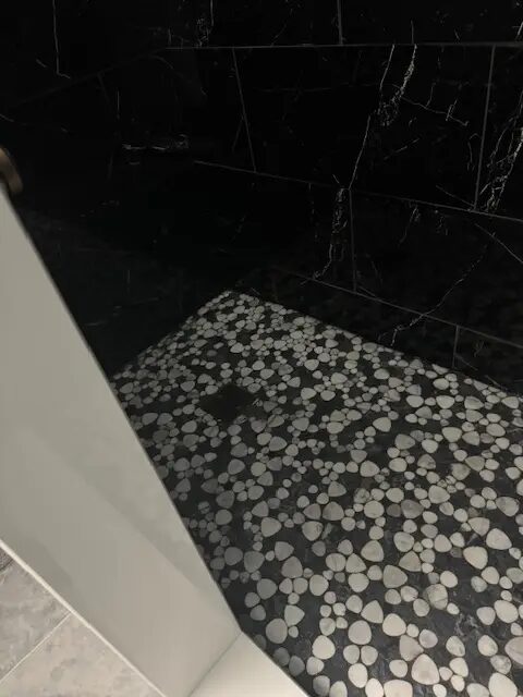 Close-up of pebble shower flooring and black tile walls