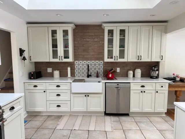 Completed white cabinetry wall with a farmhouse sink, glass doors, and brick backsplash